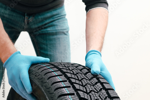 Closeup of mechanic hands pushing a black tire on a white background. Replacement of winter and summer tires. Cropped Hands Of Mechanic.