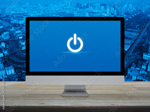 Power button icon on desktop modern computer monitor screen on wooden table over city tower, street, expressway and skyscraper, Business start up online concept