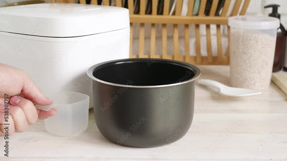 hand poring brown rice from measure cup into rice cooker bowl on wooden kitchen counter. Helthy food and eating hand poring brown rice from measure cup into rice cooker bowl on wooden kitchen counter. Helthy food and eating