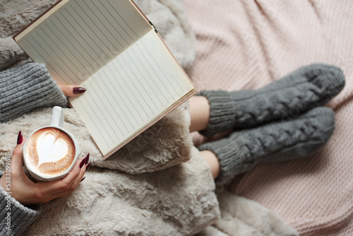 Slika na platnu Cozy home, woman covered with warm blanket, drinks coffee and reeds the book