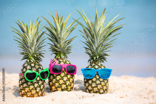 Fototapeta Naklejka Na Ścianę i Meble -  Tropical summer vacation family holiday, Pineapples wearing stylish sunglasses on the sand beach with sea background, Sunny day on the beach tropical island, summer tropical pineapple.