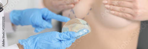 The doctor's hand holds silicone breast implant near patient