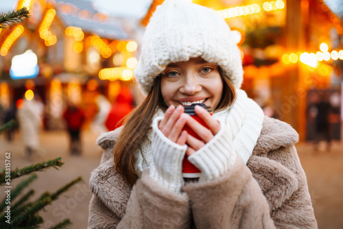 Beautiful  woman in winter style clothes posing in Christmas market decorated with holiday lights.  Winter fashion, holidays, rest, travel concept. © maxbelchenko