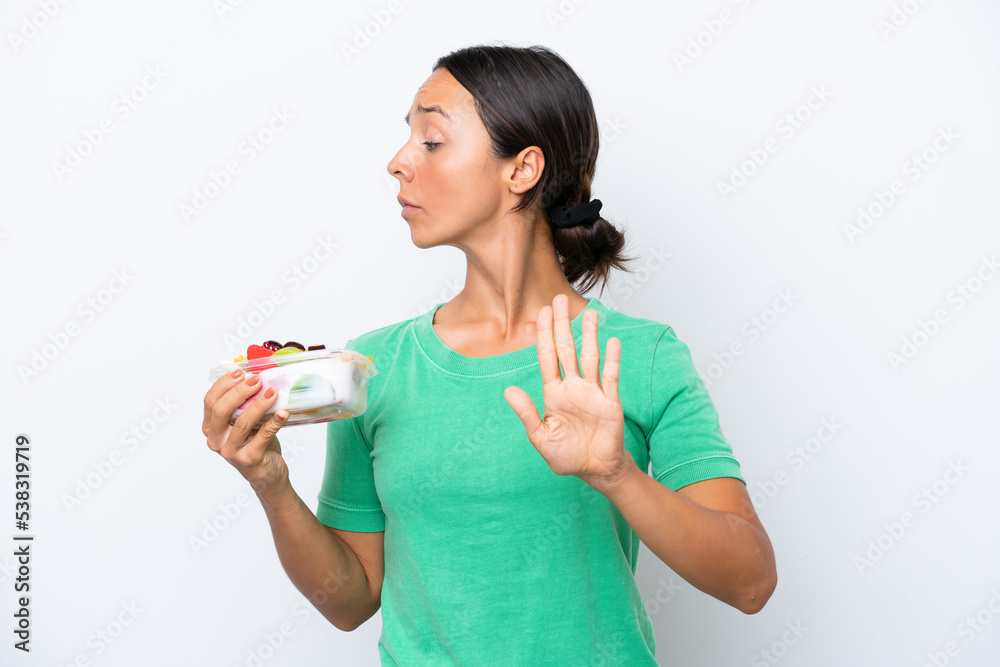 Young hispanic woman holding a bowl of fruit isolated on white background making stop gesture and disappointed Young hispanic woman holding a bowl of fruit isolated on white background making stop gesture and disappointed