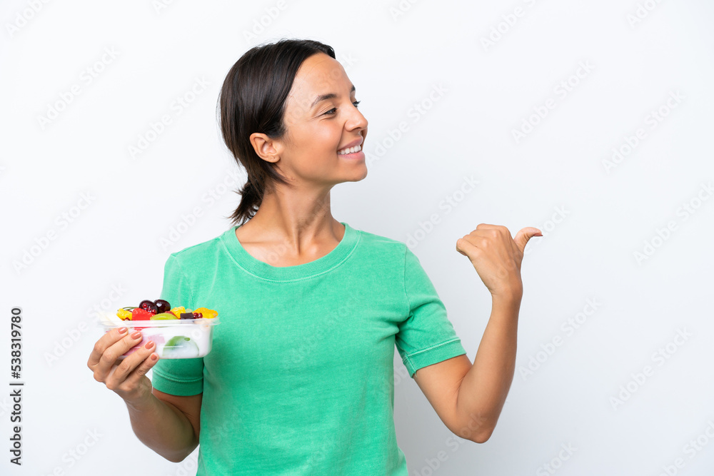 Young hispanic woman holding a bowl of fruit isolated on white background pointing to the side to present a product Young hispanic woman holding a bowl of fruit isolated on white background pointing to the side to present a product