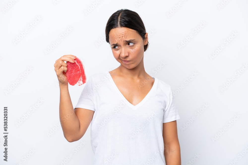 Young hispanic woman holding a piece of meat isolated on white background with sad expression Young hispanic woman holding a piece of meat isolated on white background with sad expression
