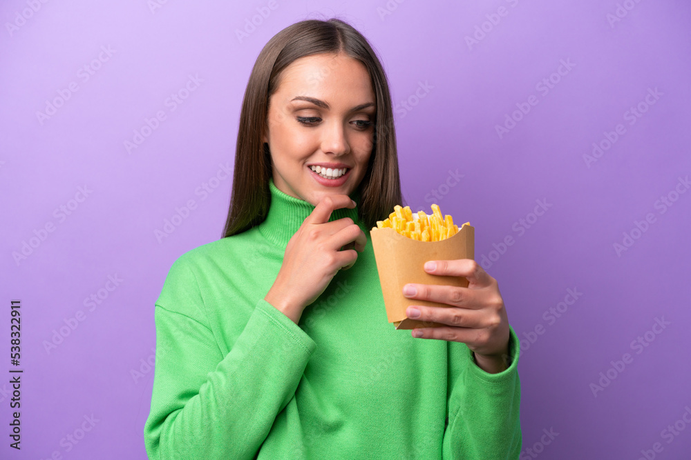 Young caucasian woman holding fried chips on purple background looking to the side and smiling Young caucasian woman holding fried chips on purple background looking to the side and smiling