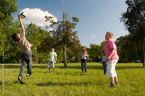 Teenagers boys and girls playing volleyball in the park on sunny spring day