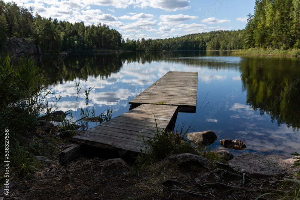 Wooden pier with the reflection of landscape and clouds in a lake in summer. Repovesi National Park, Kouvola in Finland Wooden pier with the reflection of landscape and clouds in a lake in summer. Repovesi National Park, Kouvola in Finland