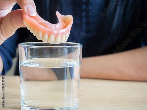 Close up hand of woman hold a acrylic dentures immersed in a glass of water
