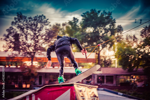 Fototapeta A guy in a yak suit at sunset jumps from a springboard on a wakeboard in an extreme park in Kiev