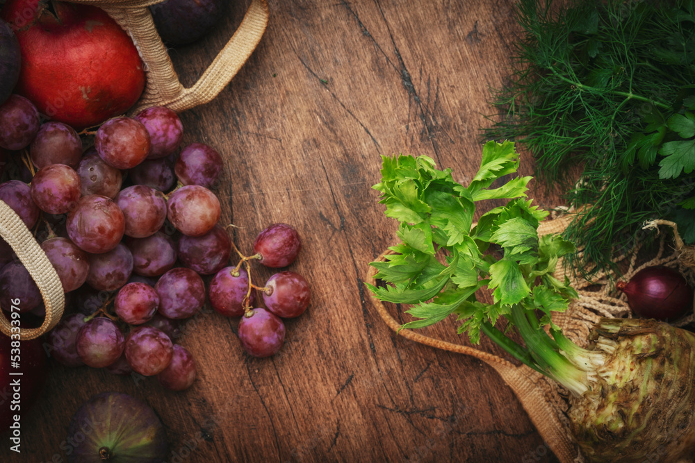 Autumn food background with vegetables, root crops and fruits in string bag: celery, carrots, apples, pomegranate, figs, grapes. Harvesting, local farm market shopping, healthy eating concept. Autumn food background with vegetables, root crops and fruits in string bag: celery, carrots, apples, pomegranate, figs, grapes. Harvesting, local farm market shopping, healthy eating concept.