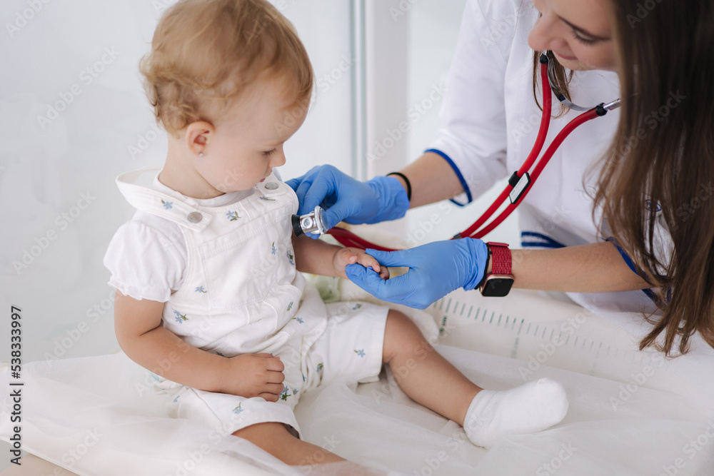 Female doctor checking child's lungs during checkup at home. Woman pediatrician using stethoscope to examine breathing and heartbeat of young patient Female doctor checking child's lungs during checkup at home. Woman pediatrician using stethoscope to examine breathing and heartbeat of young patient