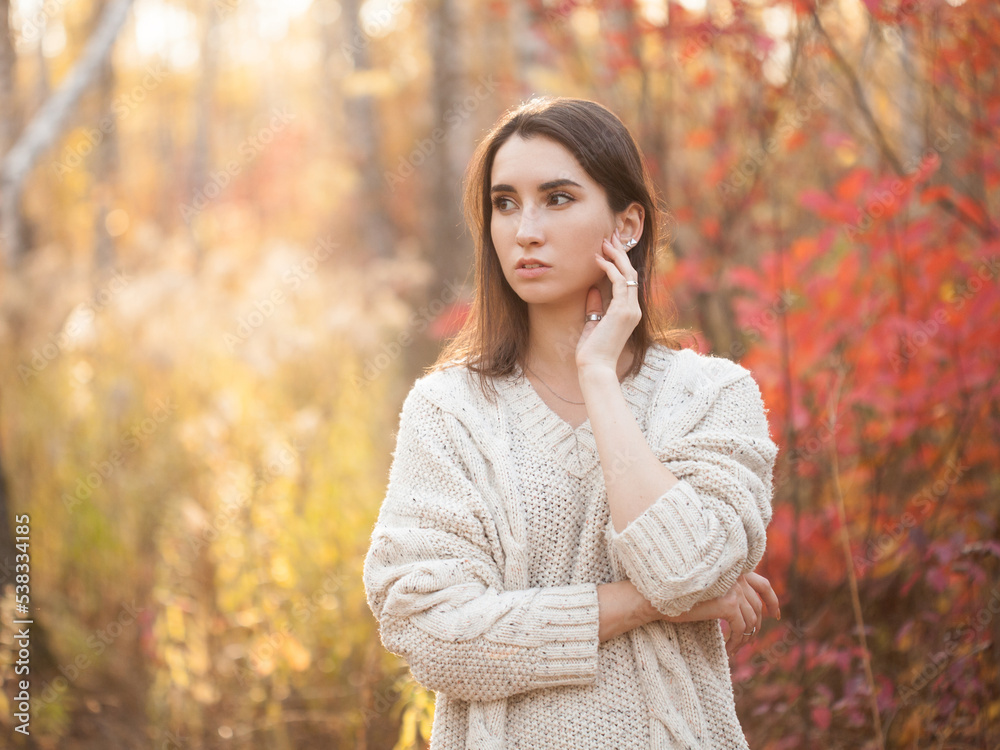 Cute young woman in white sweater standing in autumn forest Cute young woman in white sweater standing in autumn forest