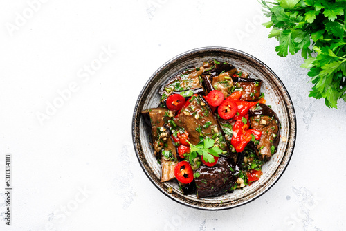 Grilled spicy eggplant with hot red chili peppers, soy sauce, garlic and sesame seeds in asian style, white table background, top view