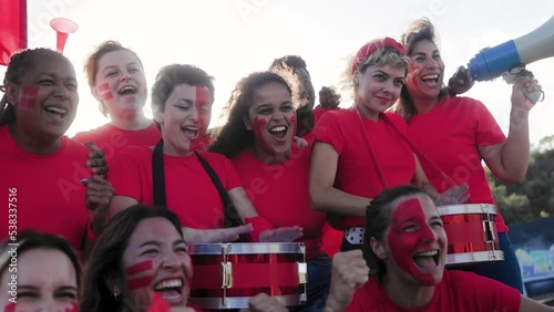 Multiracial red sport football fans celebrating with crowd cheering team on stadium tribune - Soccer spectators watching match game during world championship event photo