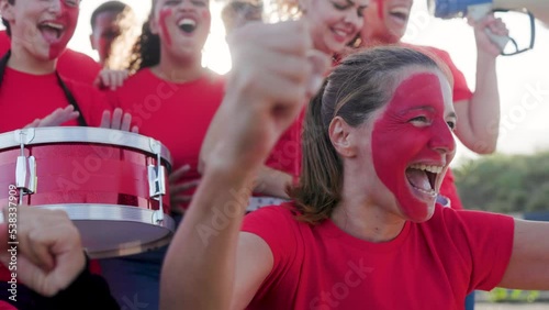 Multiracial football fans celebrating and supporting their red sport team watching the game on stadium tribune - Soccer supporters screaming during world championship event photo