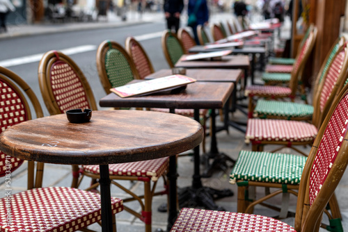 Empty chairs and tables topped with a menus and ashtrays at a sidewalk in Paris, France