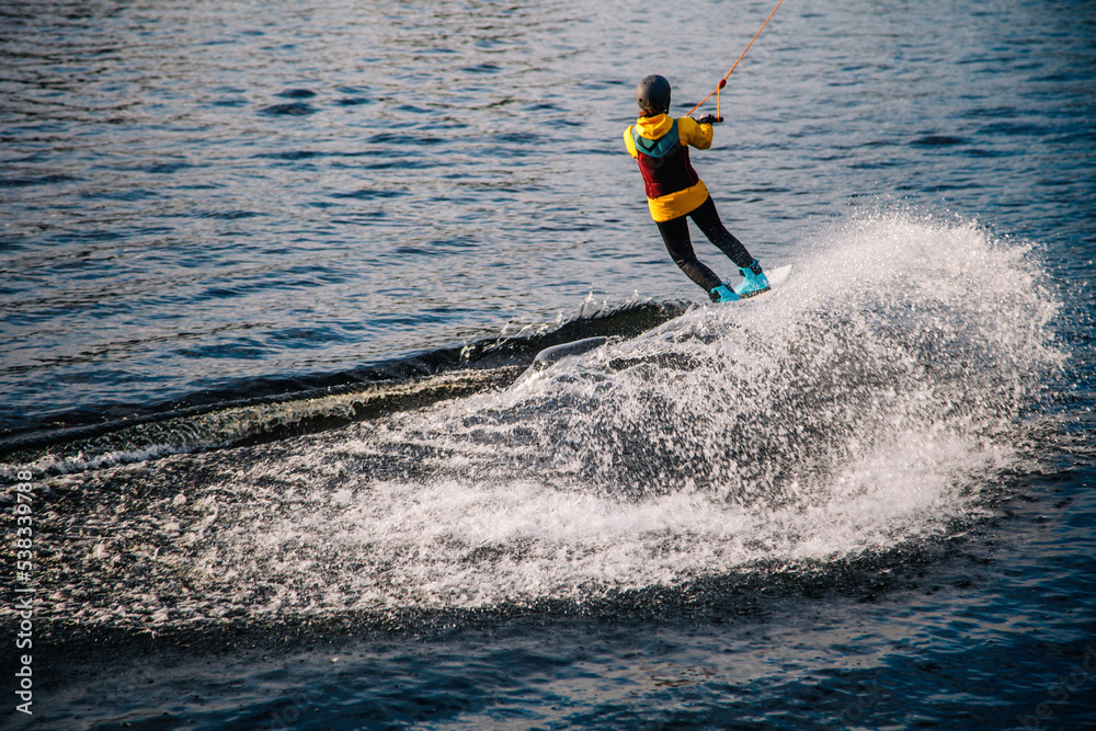 A guy in a yak suit at sunset jumps from a springboard on a wakeboard in an extreme park in Kiev. Ukraine.