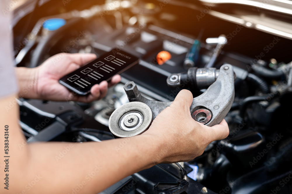 Car service concept and technology, Close up hand service technician holding engine belt tension of car spare part and use smartphone check damage point on smart checklist digital technology Car service concept and technology, Close up hand service technician holding engine belt tension of car spare part and use smartphone check damage point on smart checklist digital technology