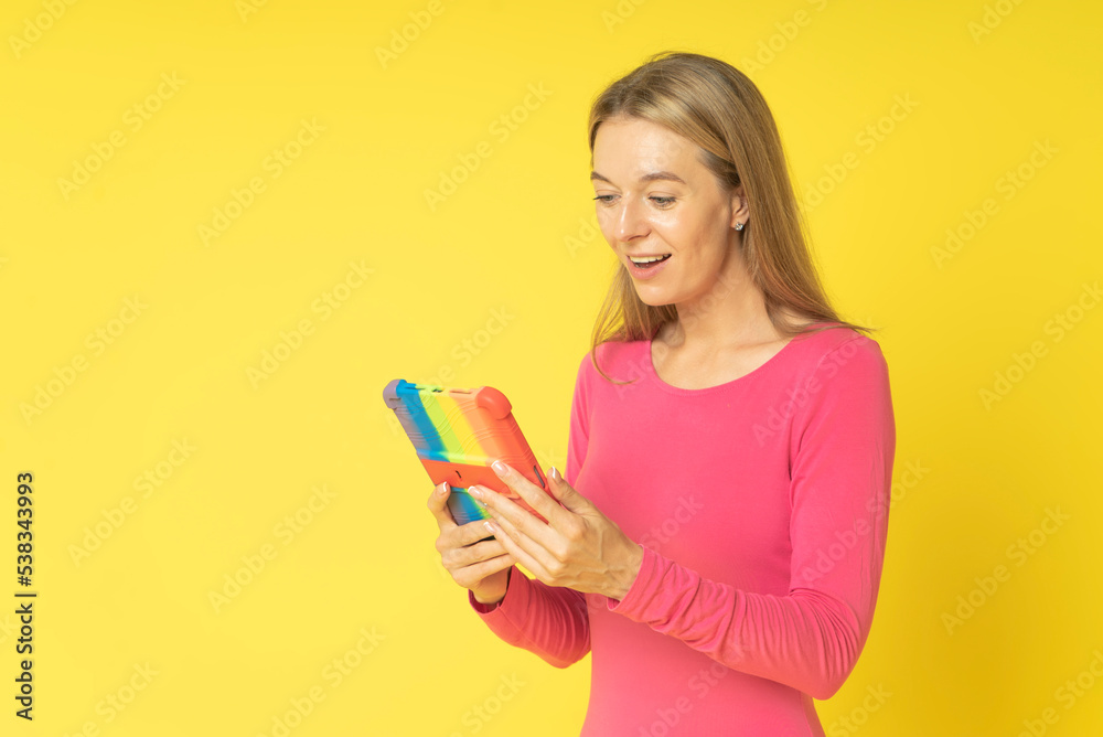 Happy attractive young woman holding digital tablet with colored cover reading online social media news, smiling woman doing internet shopping using gadget pc isolated on yellow studio background Happy attractive young woman holding digital tablet with colored cover reading online social media news, smiling woman doing internet shopping using gadget pc isolated on yellow studio background