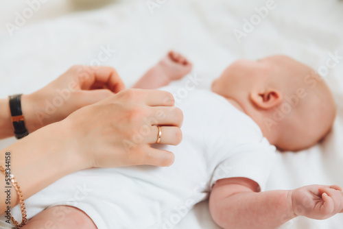 the baby is lying on the bed for 2 months, the mother's hand on the baby's stomach. newborn baby