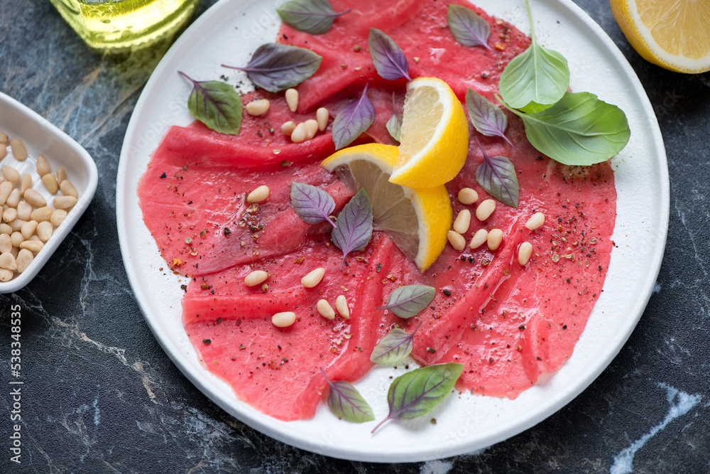 White plate with carpaccio beef on a black marble background, middle close-up, horizontal shot, selective focus White plate with carpaccio beef on a black marble background, middle close-up, horizontal shot, selective focus