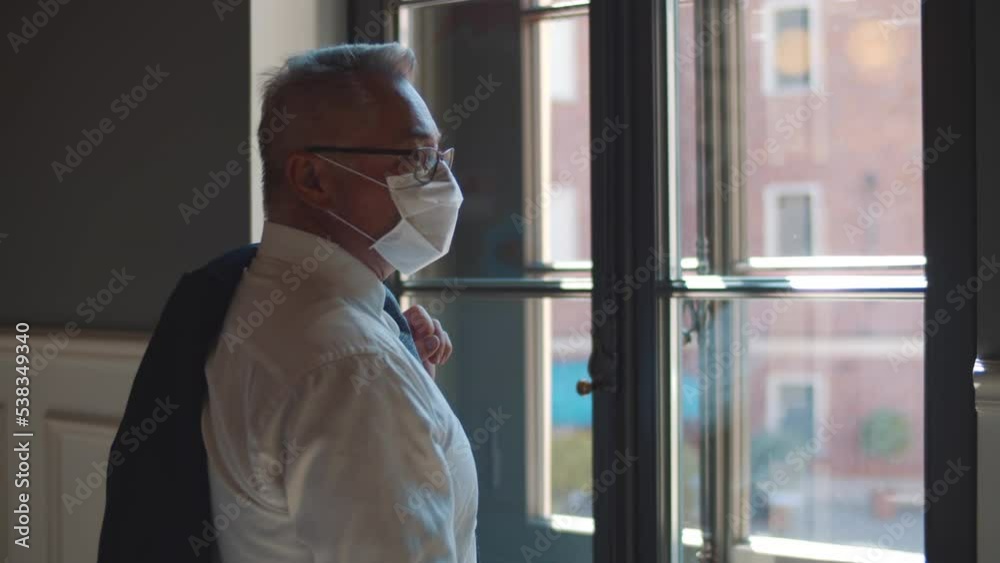 Mature businessman n safety mask standing near window in old business center. Realtime Mature businessman n safety mask standing near window in old business center. Realtime