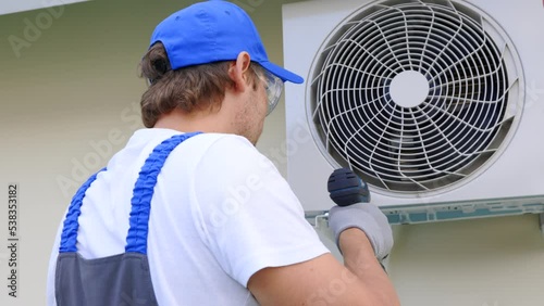 Master of service with a screwdriver fixes the mount for the outdoor unit of the air conditioner. Professional worker uses tools when installing air conditioning equipment outside the building