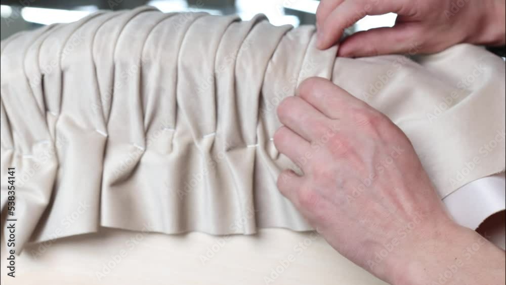 Process of pleating or draping beige fabric by hand on a furniture pouf. The process of manufacturing exclusive upholstered furniture on an individual order. Slow motion video in 4k format Process of pleating or draping beige fabric by hand on a furniture pouf. The process of manufacturing exclusive upholstered furniture on an individual order. Slow motion video in 4k format