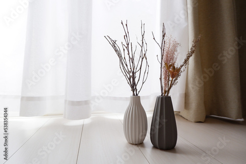 White and gray vase on a natural white wooden floor with white dried flowers in a room. autumn and winter interior image photo.