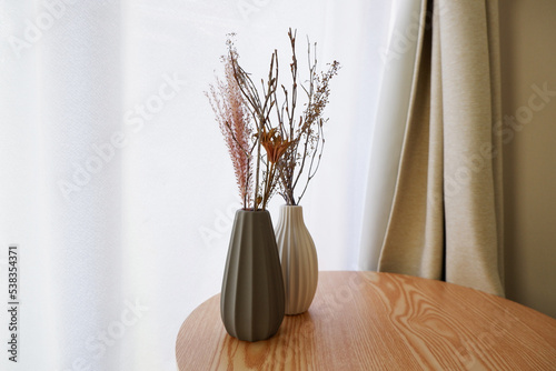 White and gray vase on a natural brown wooden table with white dried flowers in a room. autumn and winter interior image photo. 