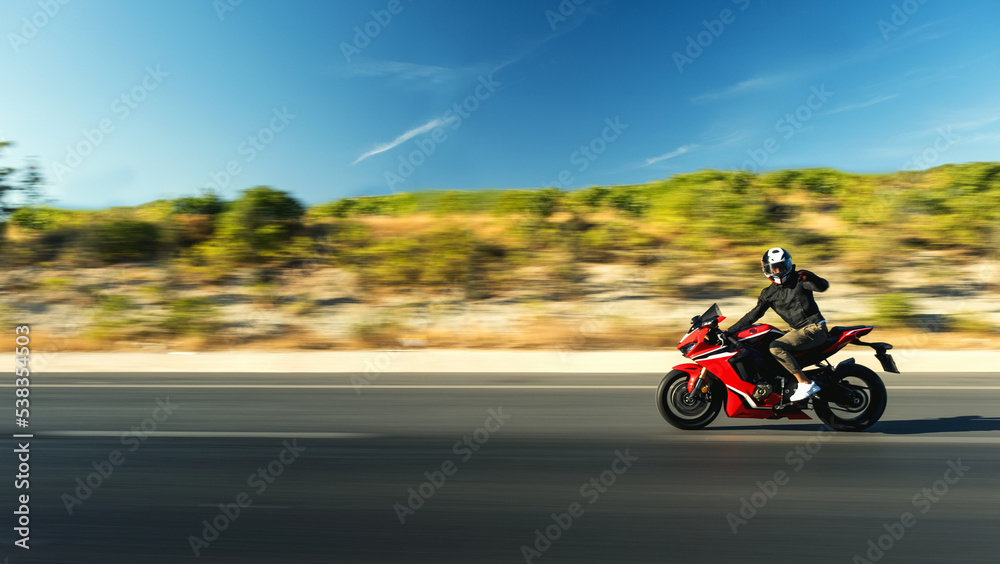 Side view of a motorcycle rider riding red race motorcycle on the highway with motion blur.