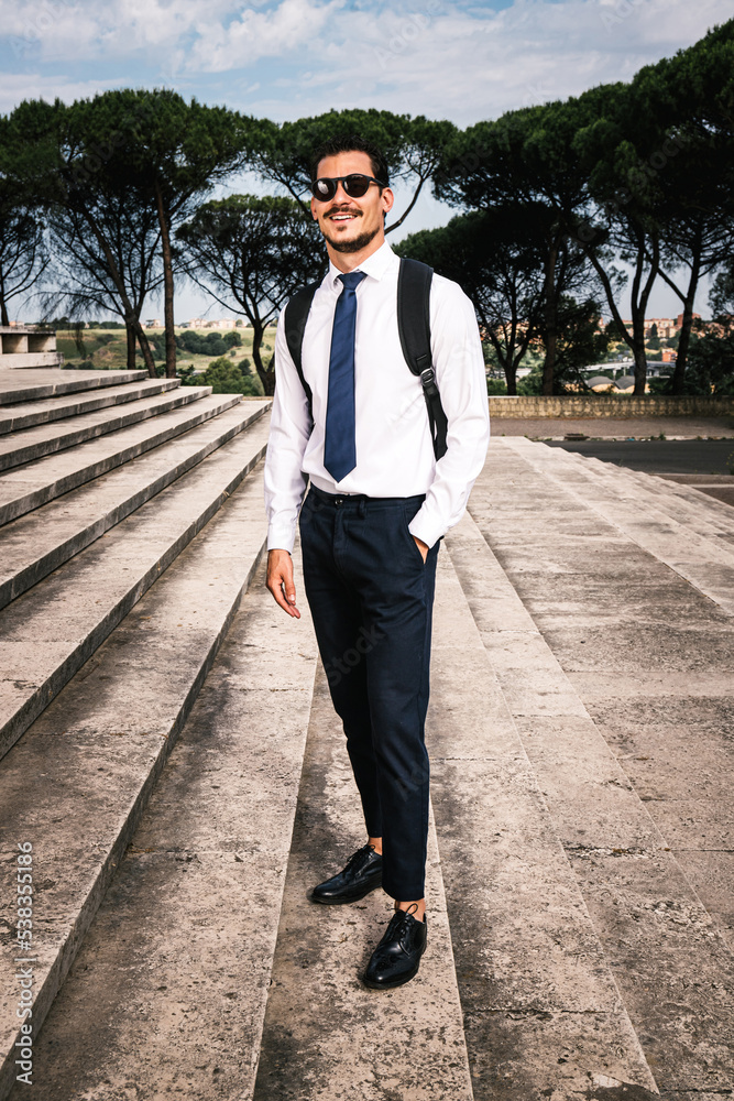 Beautiful businessman is posing on the travertine stairs before entering the office. The young businessman is going to a business meeting.