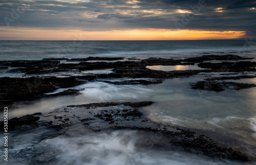 Sunset on a rocky coast with dramatic cloudy sky.
