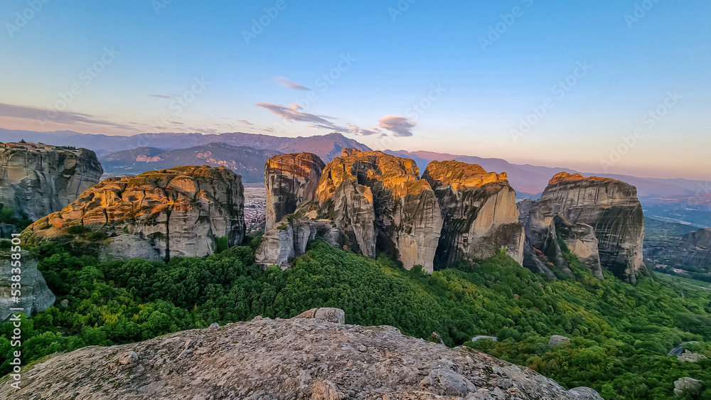 Early morning aerial panoramic view during sunrise of the rock formation complex of Meteora in Kalambaka, Meteora, Thessaly, Greece, Europe. Sun on dramatic moss overgrown rock pinnacles of Meteora