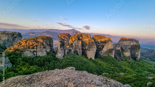 Early morning aerial panoramic view during sunrise of the rock formation complex of Meteora in Kalambaka, Meteora, Thessaly, Greece, Europe. Sun on dramatic moss overgrown rock pinnacles of Meteora