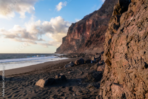 Scenic view during sunset on the volcanic sand beach Playa del Ingles in Valle Gran Rey, La Gomera, Canary Islands, Spain, Europe. Massive cliffs of the La Mercia range. Close up on Rock formation