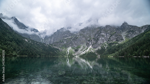 Fototapeta Naklejka Na Ścianę i Meble -  clouds quickly float over the tops of the mountains and are reflected in the water