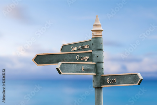 sometimes change is good four word quote written on fancy steel signpost outdoors by the sea. Soft Blue ocean bokeh background.