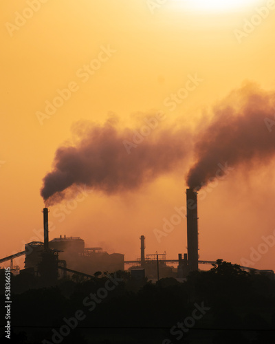 Aerial view of high smoke stack with smoke emission. Plant pipes pollute atmosphere. silhouette background.