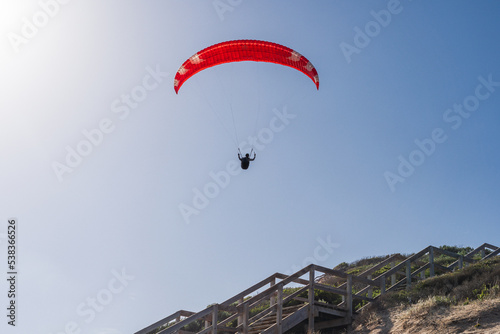 A parasailer silhouetted high above a staircase in a bright blue sky