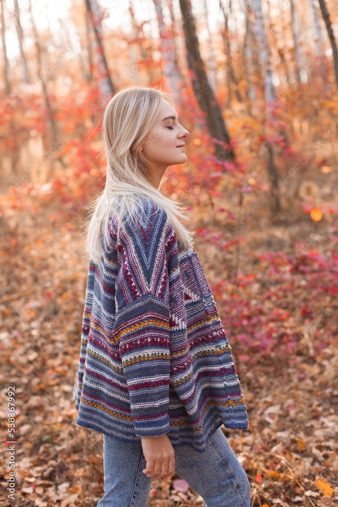 Young beautiful woman in cardigan walking in the autumn forest. Eyes closed.