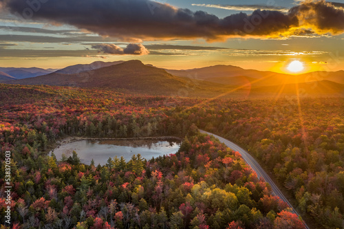 Sunrise over a scene of a road and lake through a forest with trees in fall colors of red, orange and yellow, Kancamagus Highway, White Mountains, New Hampshire photo