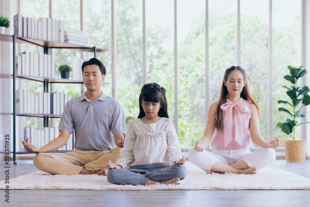 Young asian family sitting on floor doing relaxing yoga or meditation at home Young asian family sitting on floor doing relaxing yoga or meditation at home