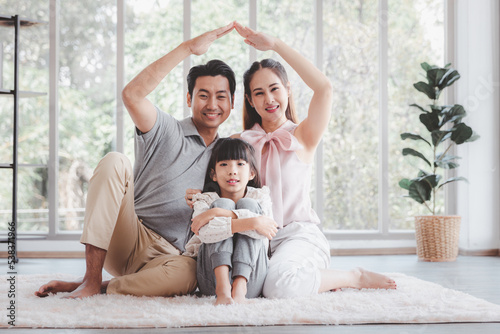 Happy young asian family father mother making hands shape house roof with little cute daughter at home. Family relocation or insurance protecting concept
