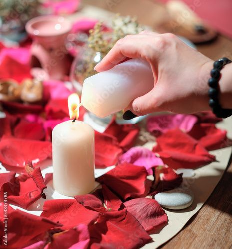 woman lighting a candle over rose petal background. stones, herbs and candles during spiritual practice. magical rituals, spiritualistic and channeling session photo