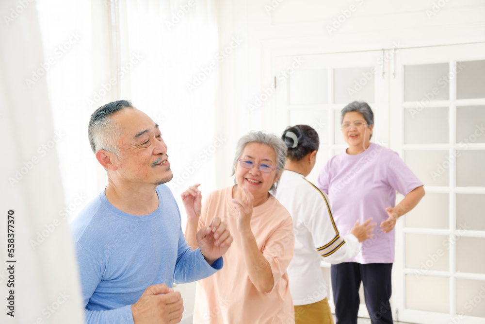 Obraz premium Active Asian senior group mix with man and woman exercise by dancing together at home with relaxing, smiling and laughing. Indoor activity for mature seniors and retirement people. Focus on senior man