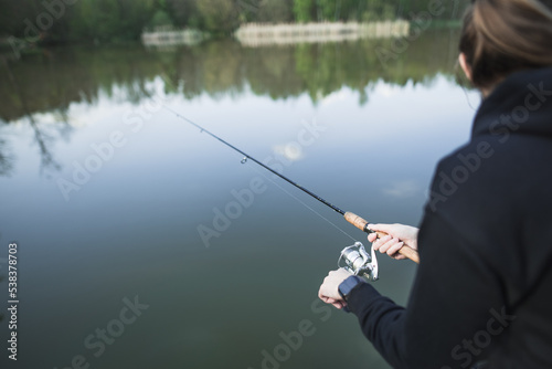 Close up on woman's hand holding fishing rod. Catching fish in nature at sunset. A relaxing hobby.