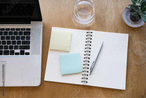 Writing on a notepad while working from home. A lap top  and plant are also on display on this brown striped working table   flat lay.